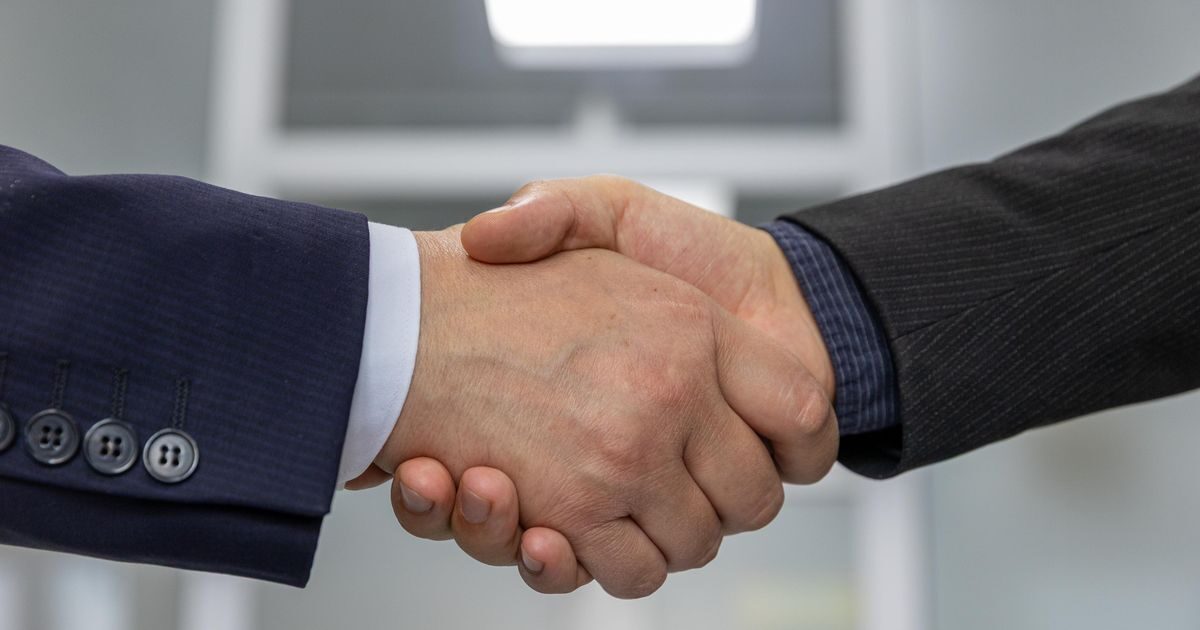Two people in business suits shaking hands to close a deal