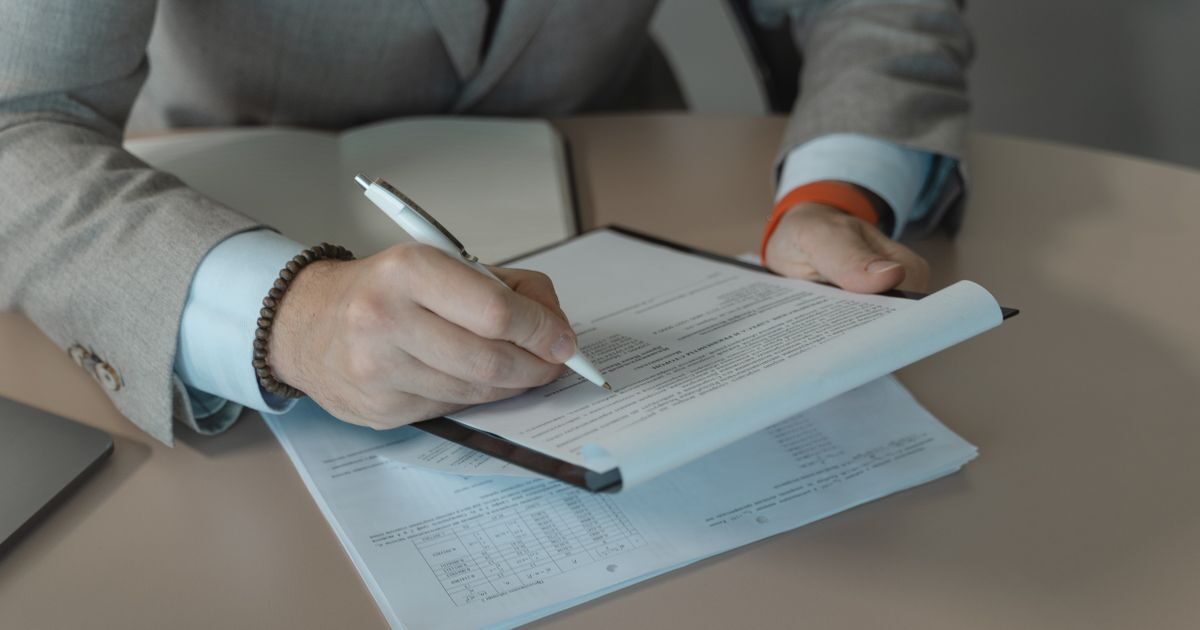 شخص يرتدي بدلة يوقّع مستنداً قانونياً بقلم
